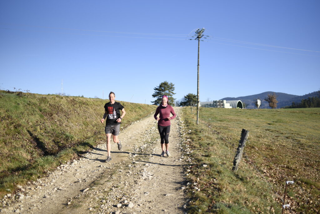 Deux coureurs en entraînement sur un chemin du Livradois‑Forez, dans un paysage rural et ensoleillé.