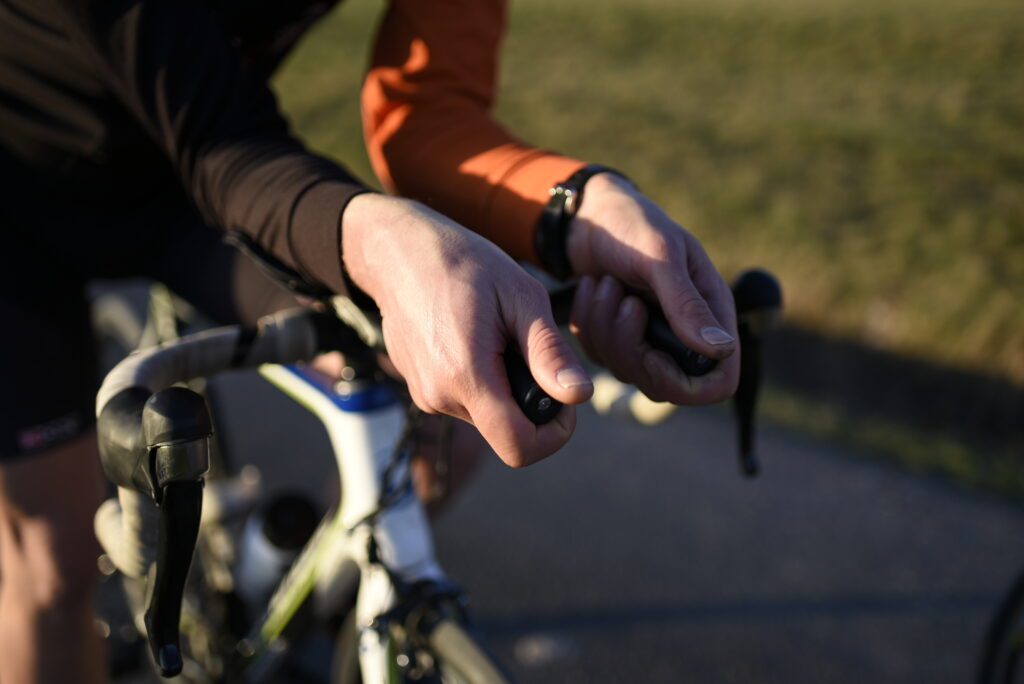“Gros plan sur les mains d’un cycliste en position aérodynamique sur un vélo de triathlon, en extérieur.
