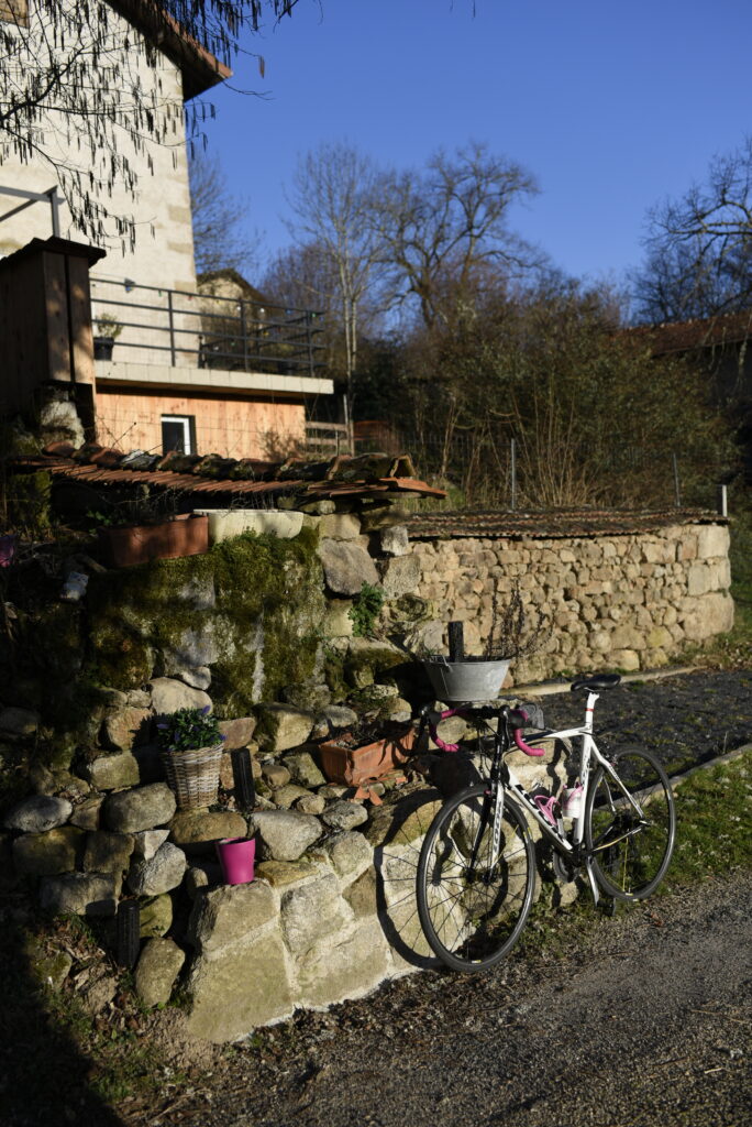 Pause vélo au Domaine de la Chouette, avec un vélo appuyé contre un muret en pierre dans un cadre rural ensoleillé.