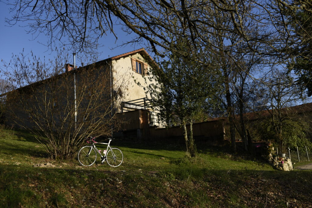 Vélo en pause sur la pelouse du Domaine de la Chouette, avec maison de campagne et arbres en arrière‑plan.