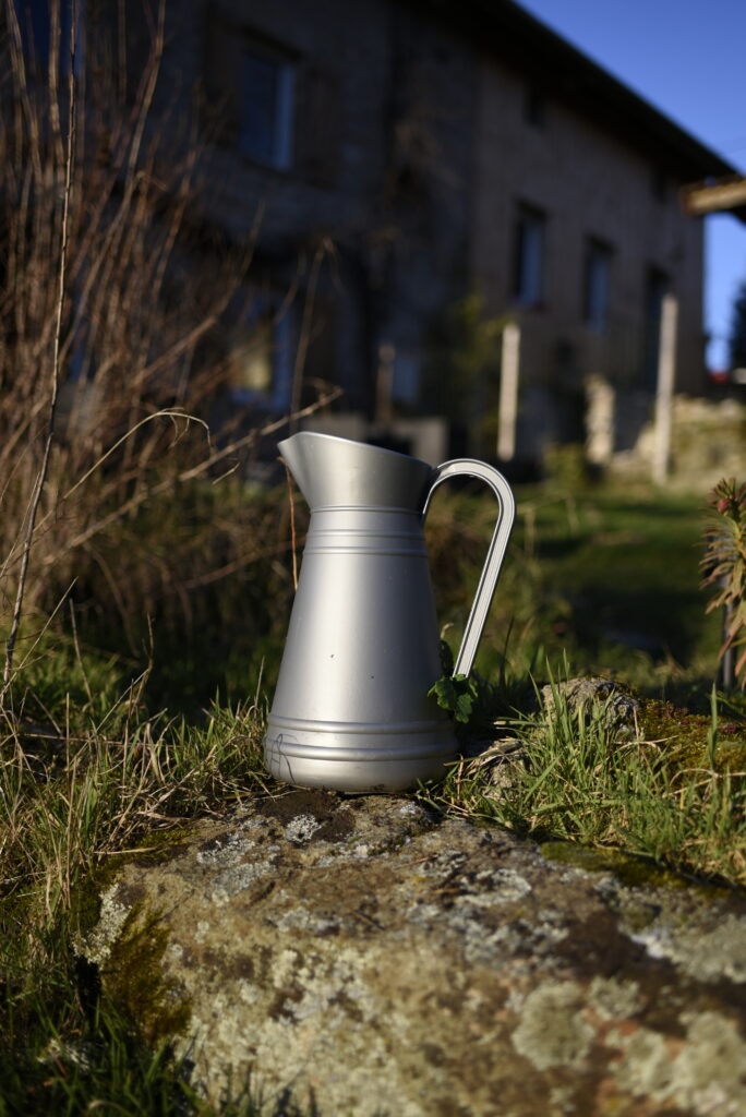 Cruche métallique sur une pierre au Domaine de la Chouette, dans un jardin baigné de lumière.