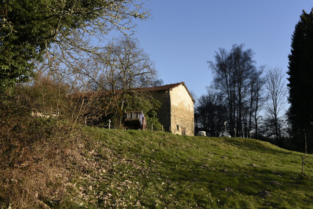 Vue du Domaine de la Chouette avec bâtiment en pierre, chariot en bois et paysage rural ensoleillé.