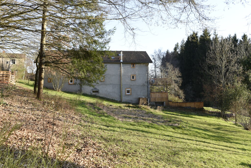 Vue du Domaine de la Chouette avec maison en pierre grise, terrasse en bois et environnement arboré.