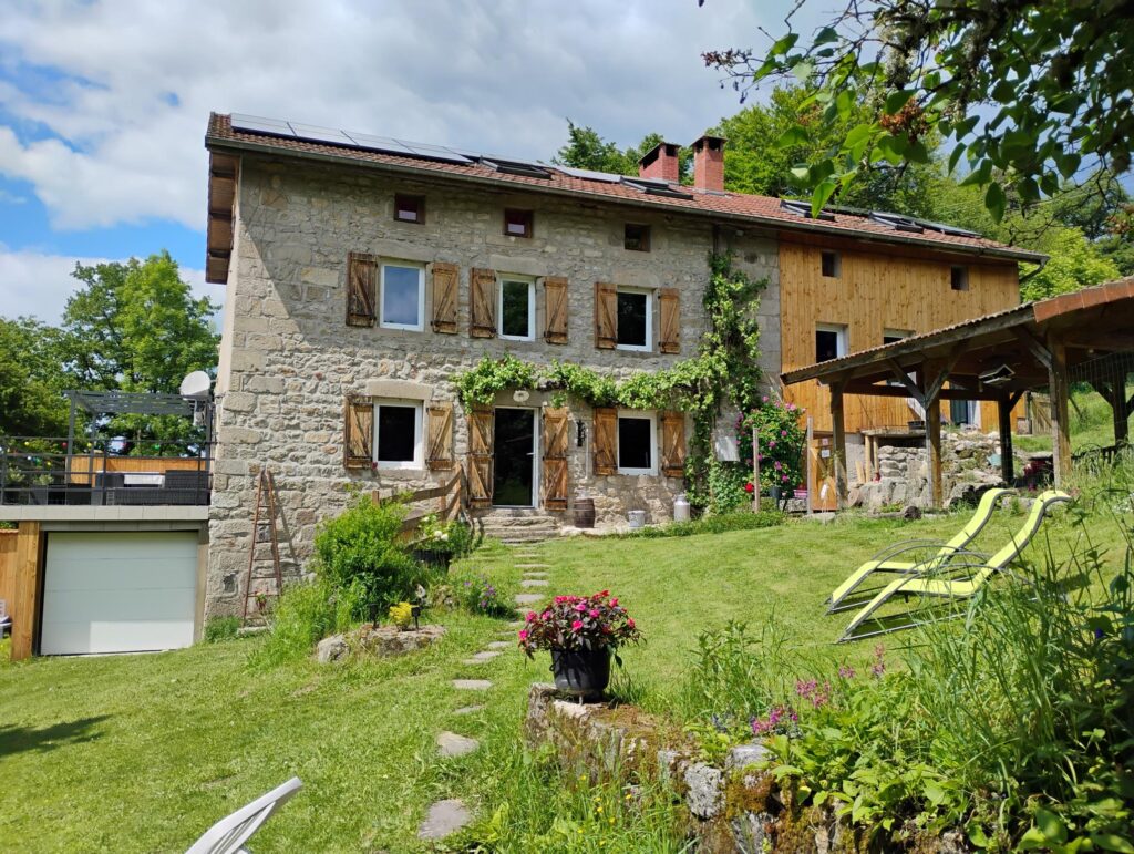 Gîte en pierre du Livradois-Forez avec jardin fleuri, terrasse bois et chaises longues.