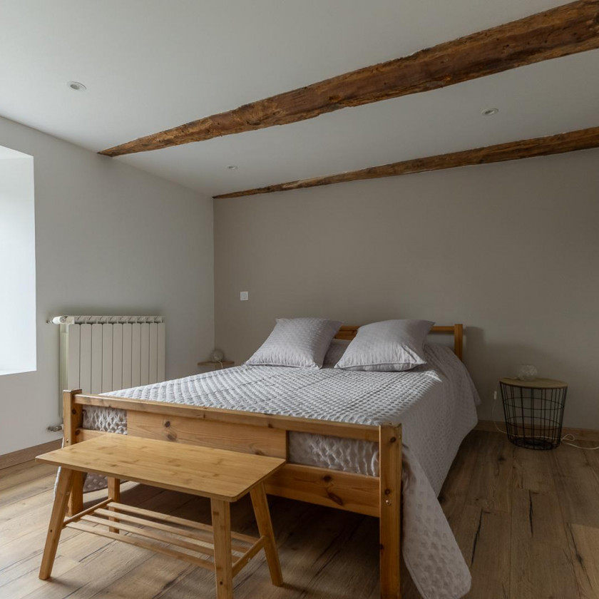 Chambre du Domaine de la Chouette avec lit double, poutres apparentes et décoration épurée.