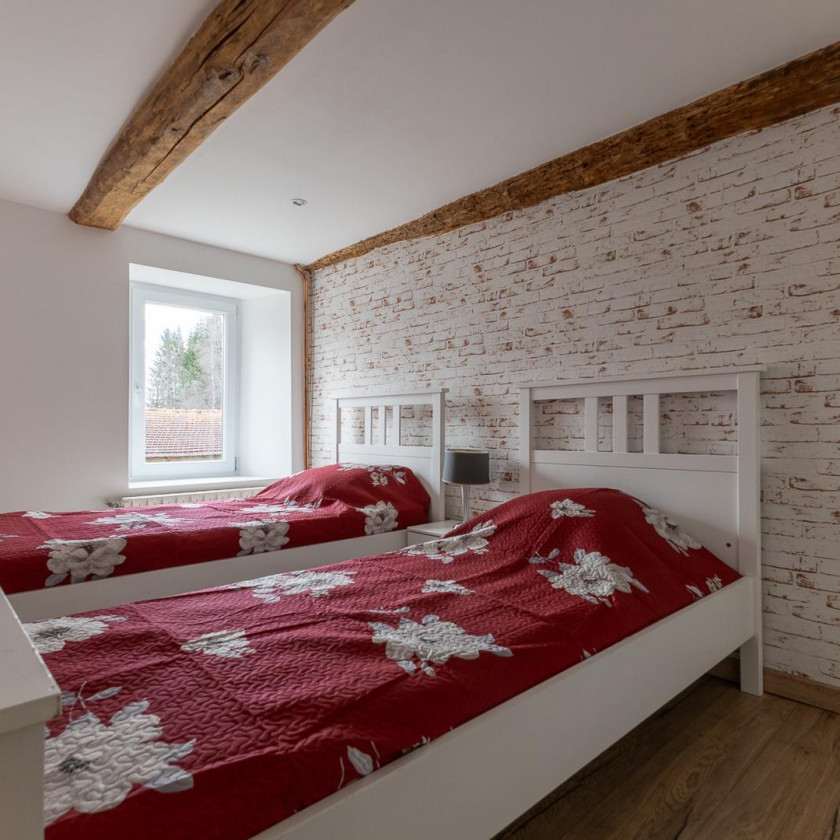 Chambre du gîte du Domaine de la Chouette avec deux lits simples, murs en pierre et poutres apparentes.