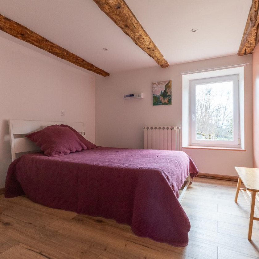 Chambre du Domaine de la Chouette avec lit simple, poutres apparentes et vue sur le jardin.