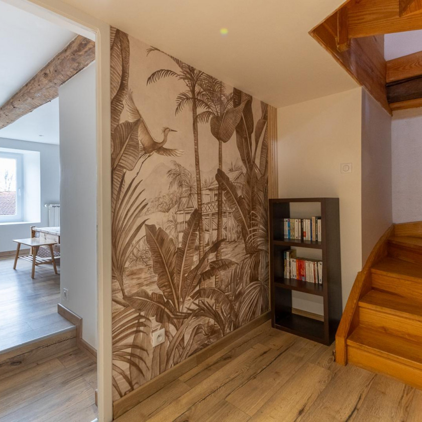 Espace intérieur du Domaine de la Chouette avec fresque tropicale, escalier en bois et coin lecture.