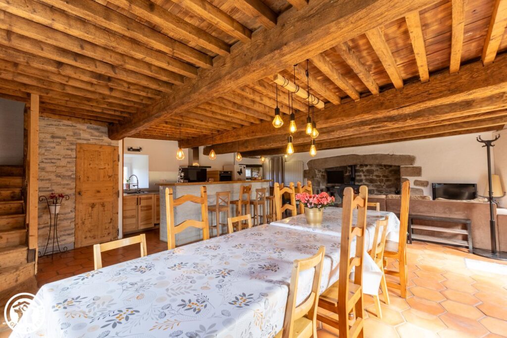 Grande pièce de vie du Domaine de la Chouette avec salle à manger, cuisine ouverte et cheminée en pierre.