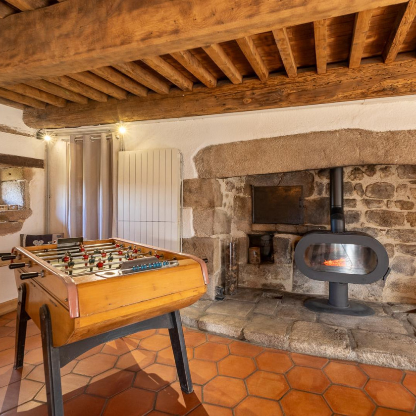 Salle de détente du Domaine de la Chouette avec baby‑foot, poêle à bois et murs en pierre.