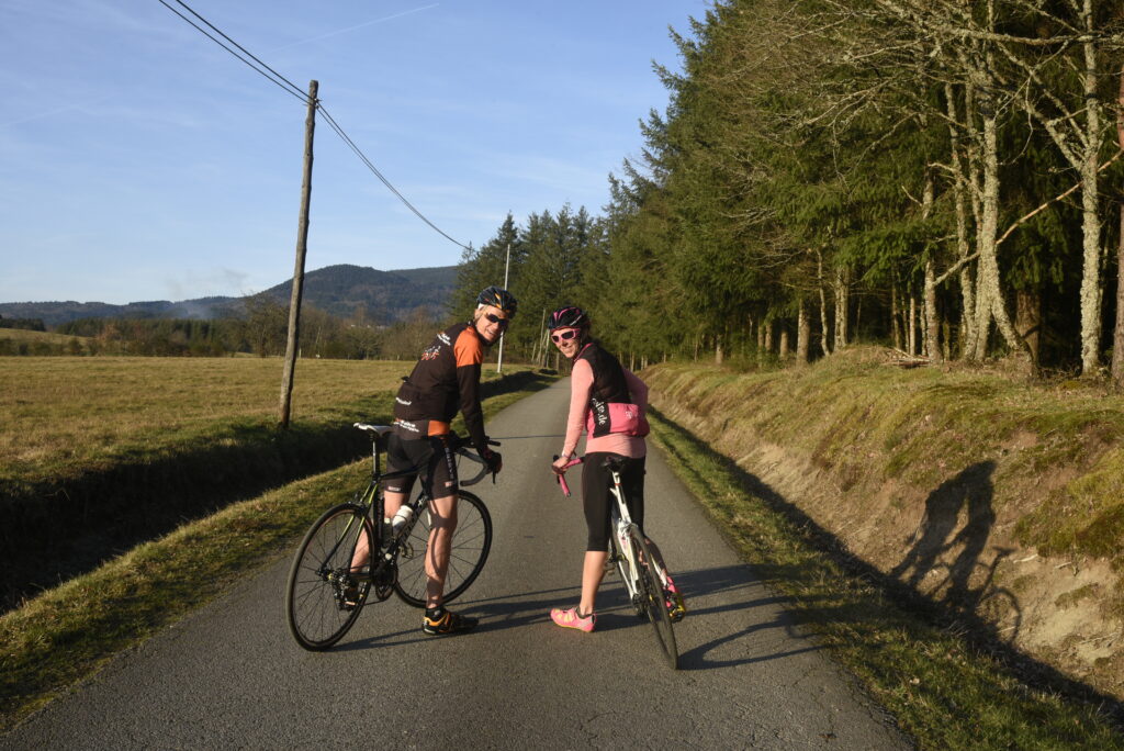 Deux cyclistes en pause sur une route du Livradois‑Forez, entourée de champs et de forêt.