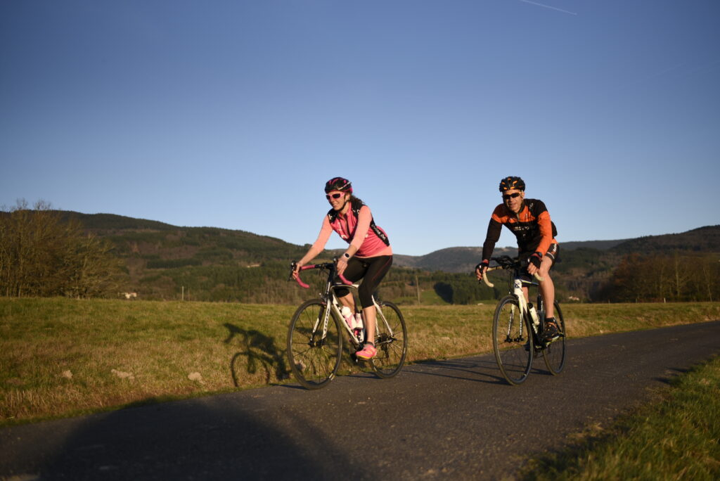 “Deux cyclistes en entraînement sur une route du Livradois‑Forez, entre champs et collines.